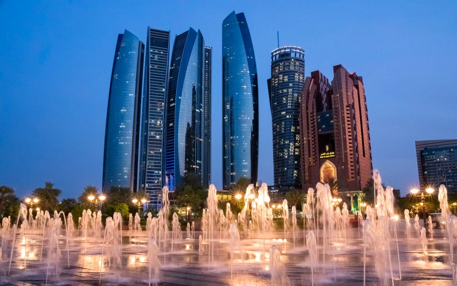 Abu Dhabi's Etihad Towers at dusk, behind a plaza of lit fountains