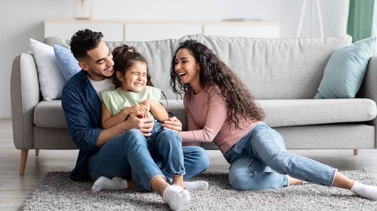 Parents and their daughter laughing together on the living-room floor